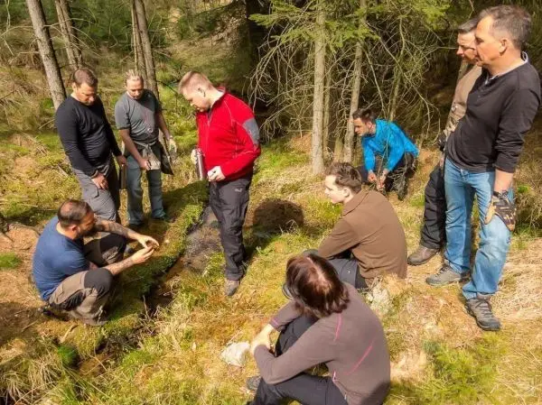 Gruppe beobachtet einen Wasserlauf im Wald, einer zeigt etwas auf dem Boden
