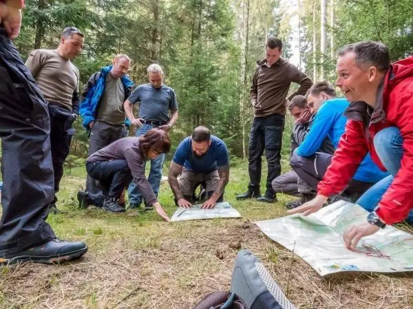 Gruppe betrachtet Karten auf dem Boden im Wald, einige knien, andere stehen