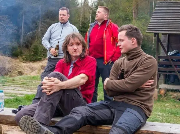 Gruppe sitzt auf einer Holzbank, einige halten Getränke in der Hand