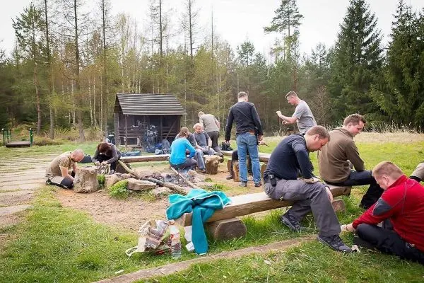 Gruppe sitzt auf Holzstämmen und arbeitet an verschiedenen Aufgaben im Freien