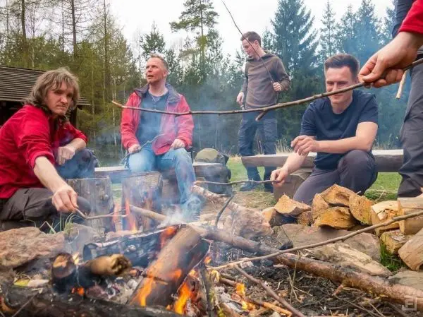 Gruppe sitzt um ein Feuer und röstet Lebensmittel auf langen Stöcken