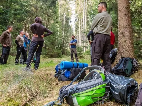 Gruppe steht im Wald um Rucksäcke, einige Personen diskutieren