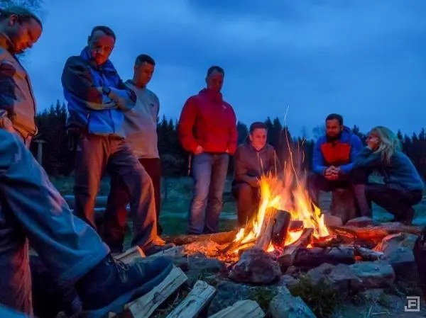 Gruppe von Personen sitzt um ein Feuer und beobachtet die Flammen