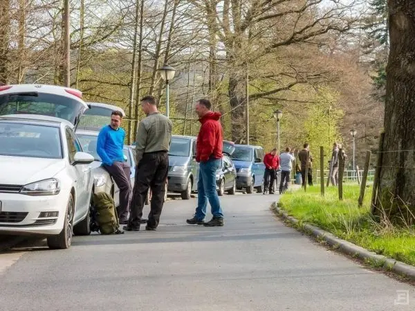 Gruppe von Personen steht an parkenden Autos und unterhält sich auf der Straße
