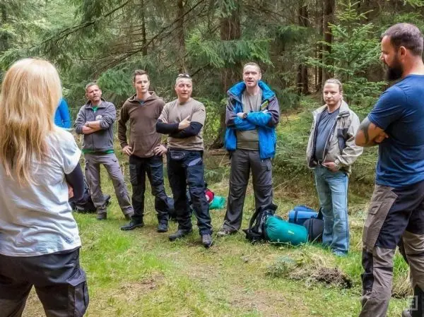Gruppe von Personen steht im Wald, einige Rucksäcke liegen auf dem Boden