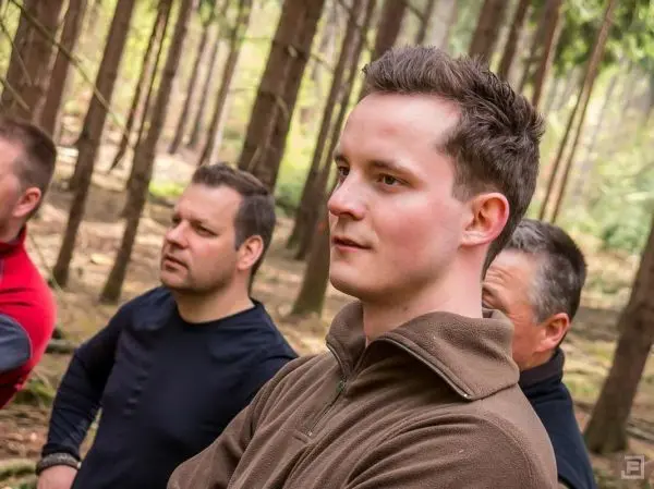 Gruppe von Personen steht im Wald und hört aufmerksam zu