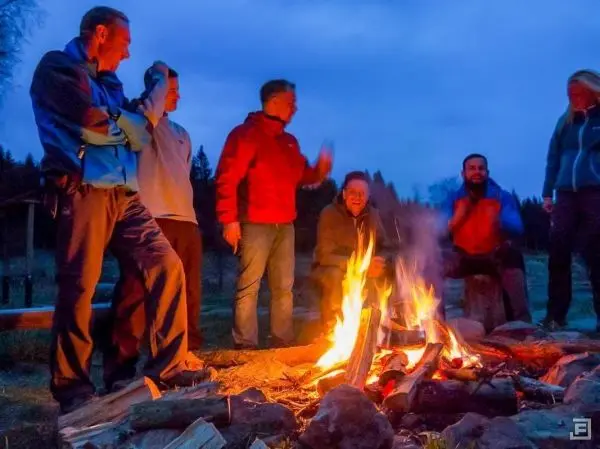 Gruppe von Personen steht um ein Feuer und unterhält sich beim Überlebenstraining