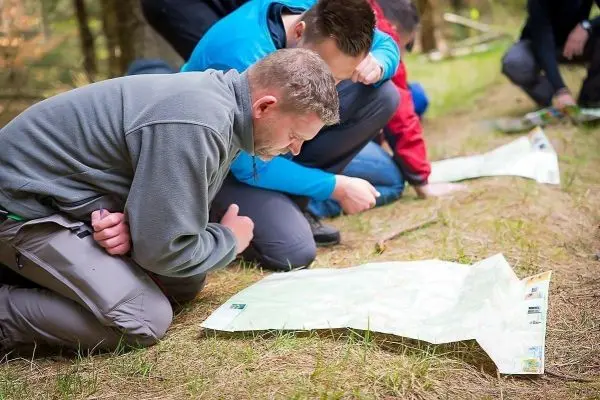 Gruppenteilnehmer knien auf dem Boden und studieren Karten im Wald