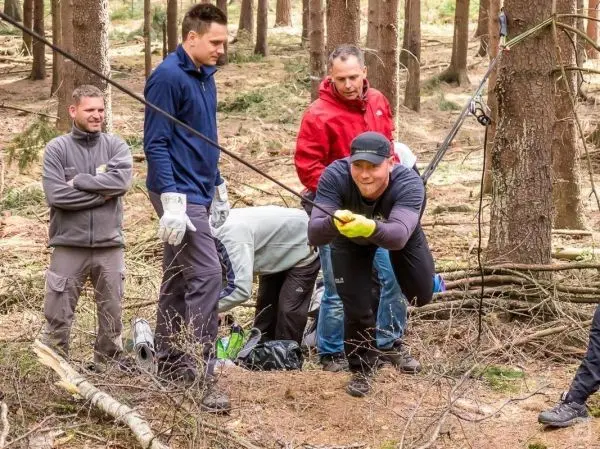 Gruppenteilnehmer ziehen an einem Seil, während andere beobachten und helfen