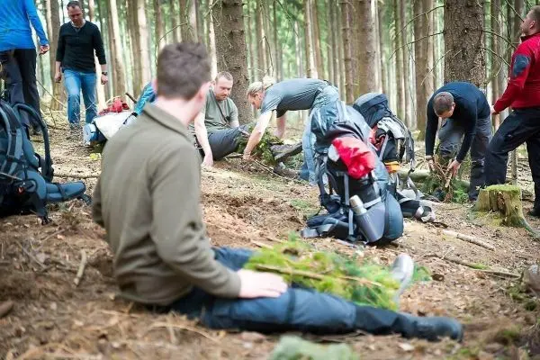 Gruppierung arbeitet im Wald an einer Holzstruktur mit Rucksäcken im Hintergrund