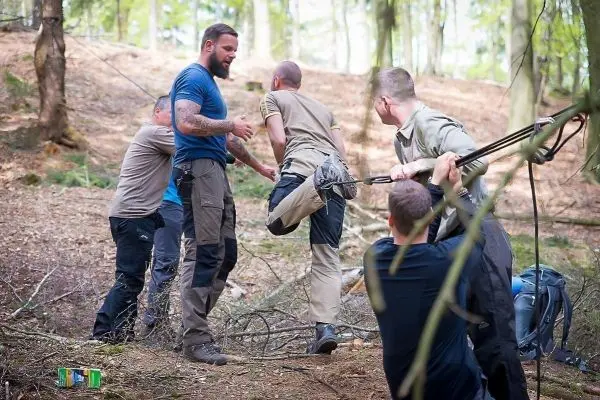 Gruppierung von Personen bei einer Seilquerung im Wald, eine Person wird unterstützt