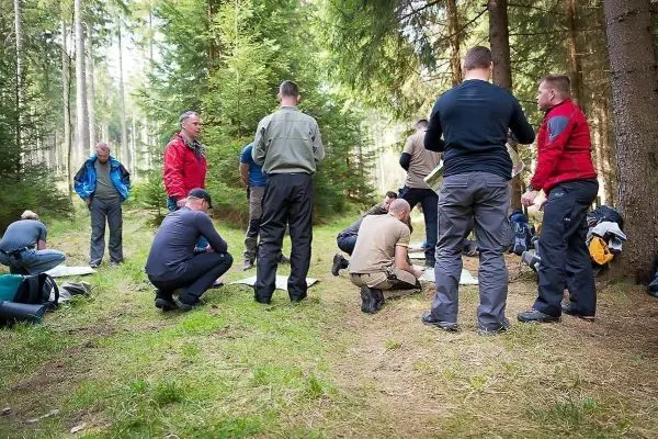 Gruppierung von Personen im Wald, einige knien und betrachten Materialien
