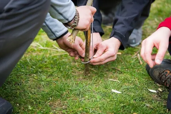 Hände binden einen Stock mit Schnur auf dem Boden