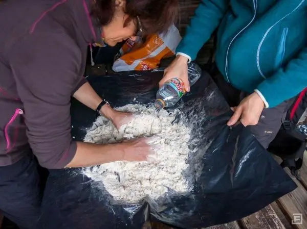 Hände kneten Mehl auf einer schwarzen Folie, während Wasser hinzugefügt wird