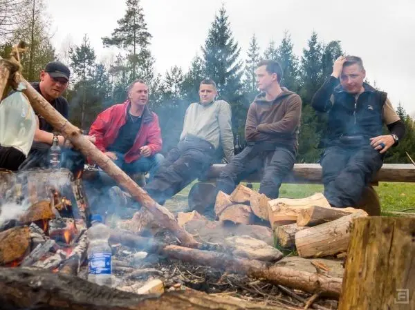 Kleines Bodenfeuer mit Holzscheiten und fünf Personen sitzen am Rand