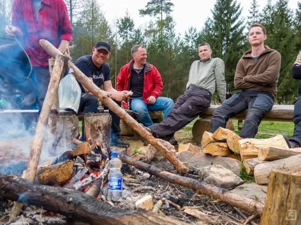 Kleines Bodenfeuer mit Holzscheiten und mehreren Personen sitzen am Lagerplatz