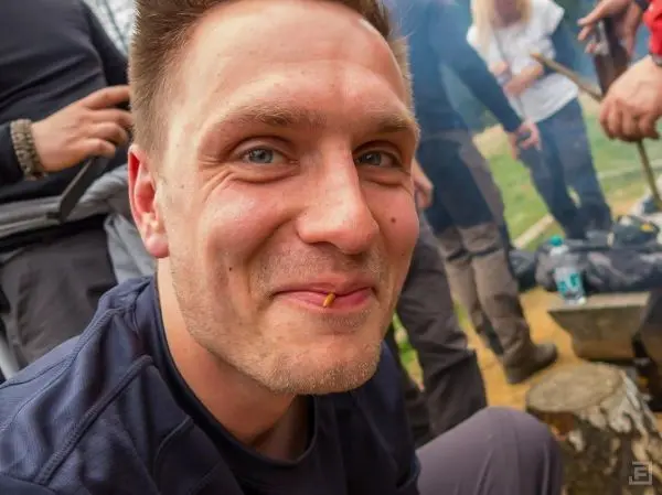 Lächelnder Mann mit Snack im Mund sitzt am Lagerfeuer