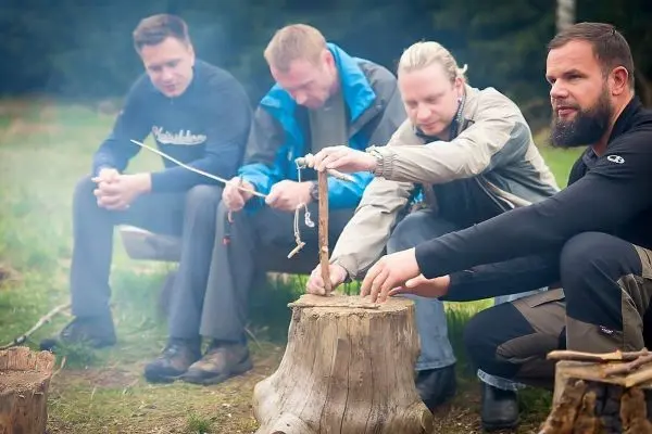Männer sitzen um einen Baumstumpf und bereiten Zunder für ein Feuer vor