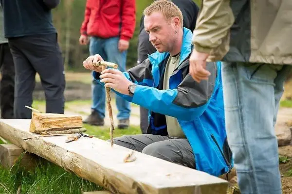 Mann bearbeitet einen Stock auf einer Holzbank mit einem Messer