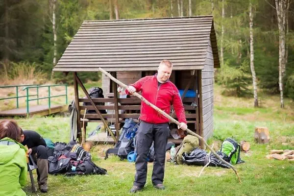 Mann bearbeitet einen Stock vor einer Holzunterkunft im Wald