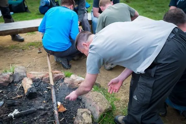 Mann beugt sich über ein kleines Bodenfeuer und prüft glühende Reste