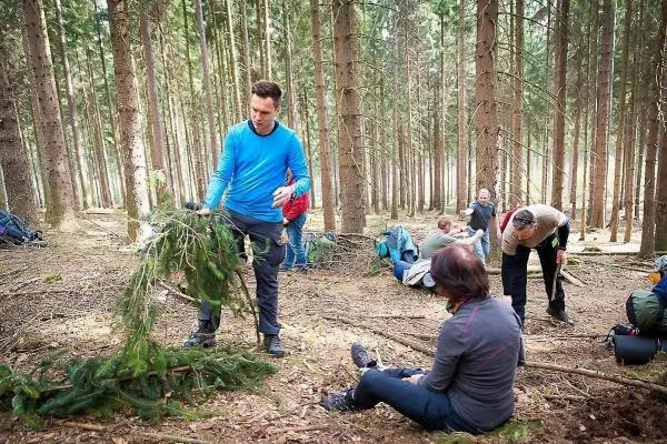 Mann hält Äste in der Hand, während andere im Wald Materialien sammeln