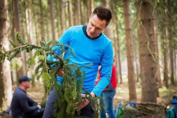 Mann hält einen Zweig mit Nadelbaumzweigen in einem Wald
