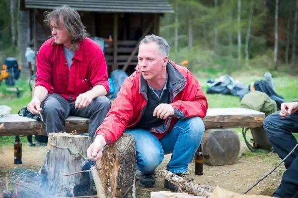 Mann hält Stock über kleines Bodenfeuer und beobachtet Flamme