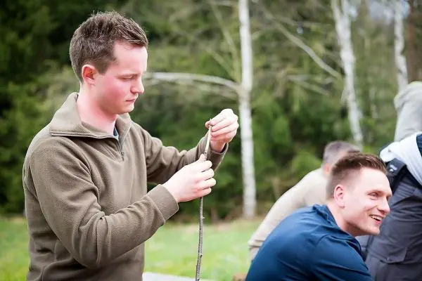 Mann knotet ein Seil in der Natur, während andere im Hintergrund sitzen