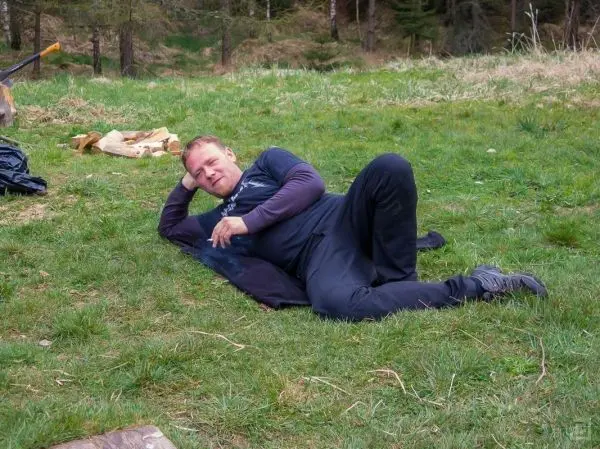 Mann liegt entspannt auf einer Matte im Gras, Holzstücke im Hintergrund