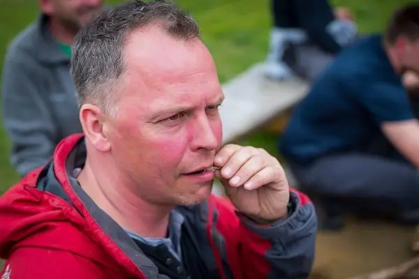 Mann mit roter Jacke hält nachdenklich eine Hand an den Mund