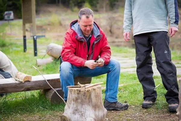 Mann schnitzt mit einem Messer an einem Holzstück auf einem Baumstumpf