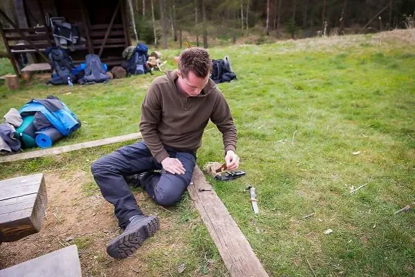 Mann sitzt auf dem Boden und schnitzt mit einem Messer an einem Holzstück