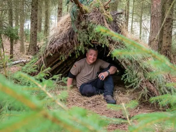 Mann sitzt in einer selbstgebauten Tarp-Notunterkunft aus Ästen und Gras