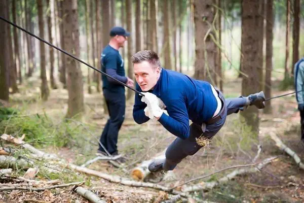 Mann überquert eine selbstgebaute Seilbrücke zwischen Bäumen