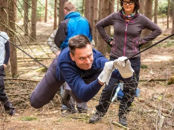 Mann überquert selbstgebaute Seilbrücke im Wald, während andere zuschauen