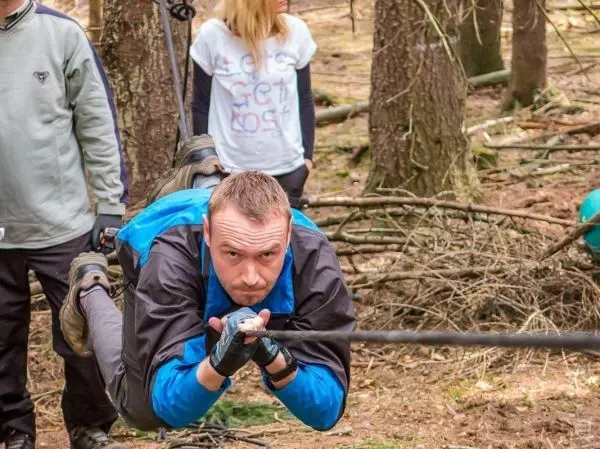 Mann überquert selbstgebaute Seilbrücke im Wald, während andere zuschauen