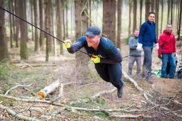 Mann überquert selbstgebaute Seilbrücke zwischen Bäumen im Wald