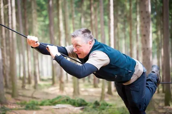 Mann überquert selbstgebaute Seilbrücke zwischen Bäumen im Wald