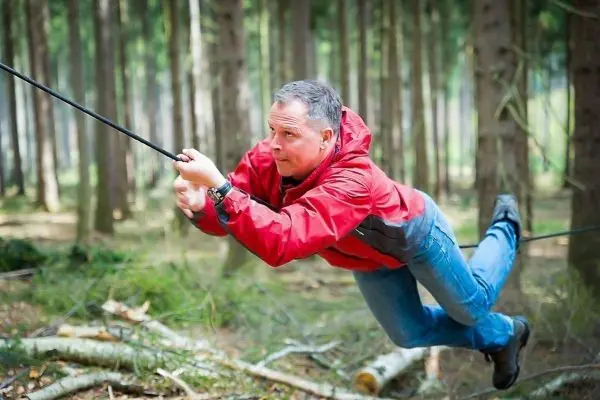 Mann überquert selbstgebaute Seilbrücke zwischen Bäumen im Wald