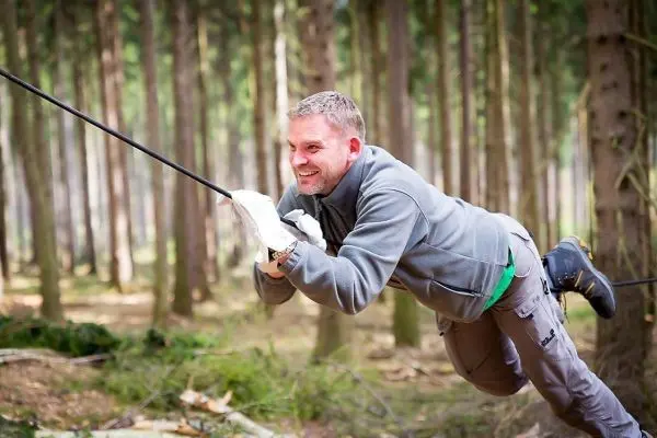 Mann überquert selbstgebaute Seilbrücke zwischen Bäumen im Wald