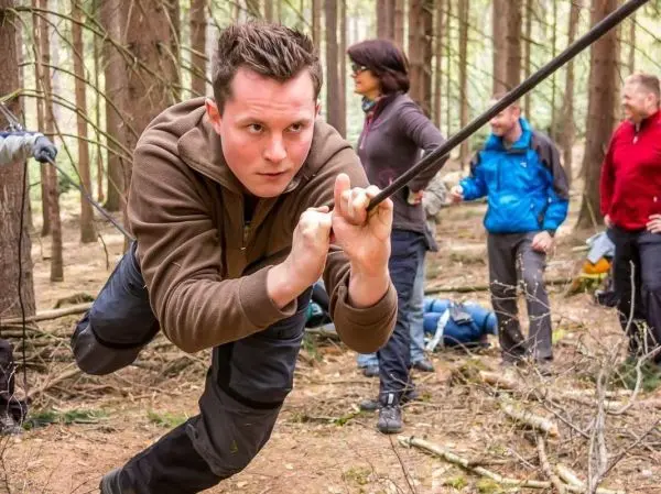 Mann überquert selbstgebaute Seilbrücke zwischen Bäumen im Wald