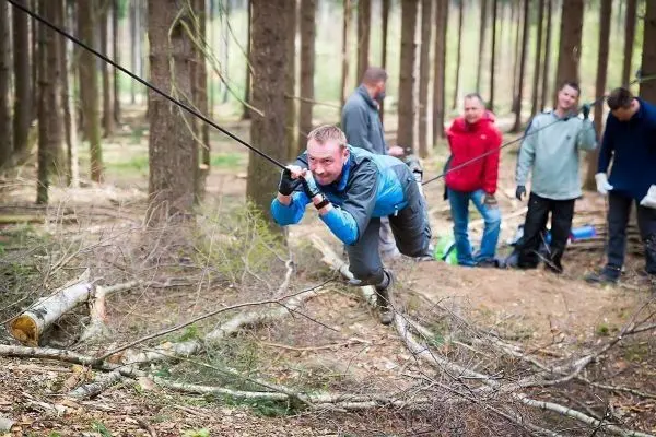 Mann überquert selbstgebaute Seilbrücke zwischen Baumstämmen im Wald