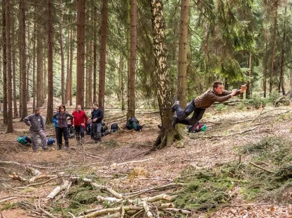Mann überquert selbstgebaute Seilbrücke zwischen zwei Bäumen im Wald