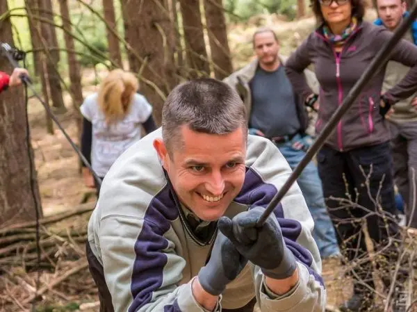 Mann zieht an einem Seil in einem Wald, mehrere Personen im Hintergrund