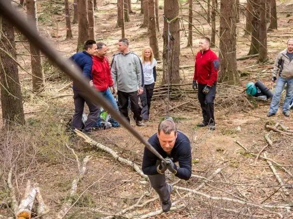Mann zieht an einem Seil in einem Wald, während andere zuschauen