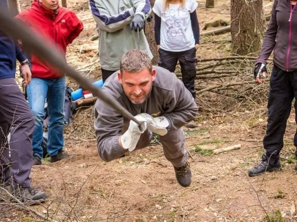 Mann zieht an einem Seil in einem Waldgebiet, um eine Seilquerung zu unterstützen
