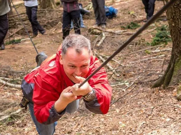 Mann zieht sich an einem Seil über den Boden in einem Waldgebiet