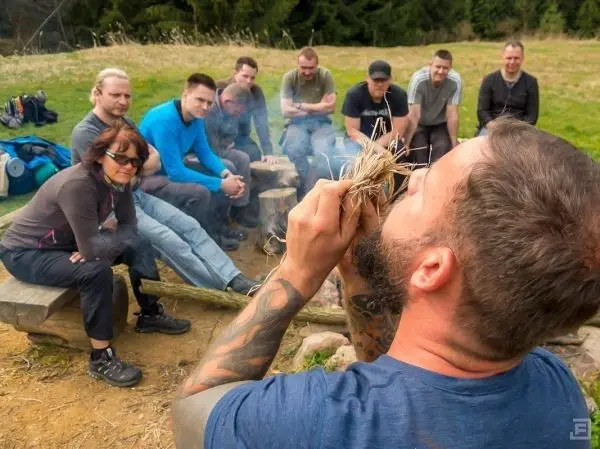 Mann zündet Zunder mit Feuerbohrer, Gruppe beobachtet aufmerksam