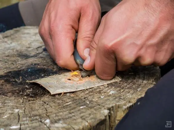 Person bearbeitet Rinde mit einem Messer auf einem Holzstück beim Überlebenstraining